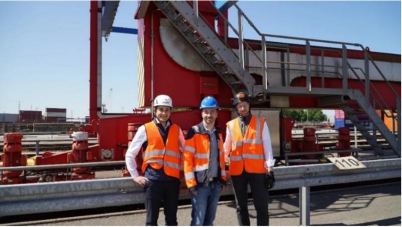 Three technicians in front of red container crane trolley at port
