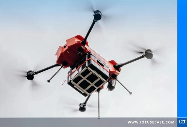 Rote Transportdrohne von Morpheus mit vier Rotoren und angehängter Transportbox im Flug, von unten vor hellem, bewölktem Himmel fotografiert