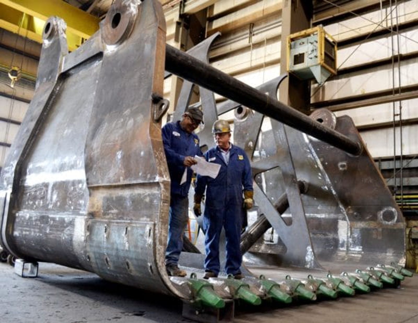 Two technicians inspect giant excavator bucket in heavy industry facility