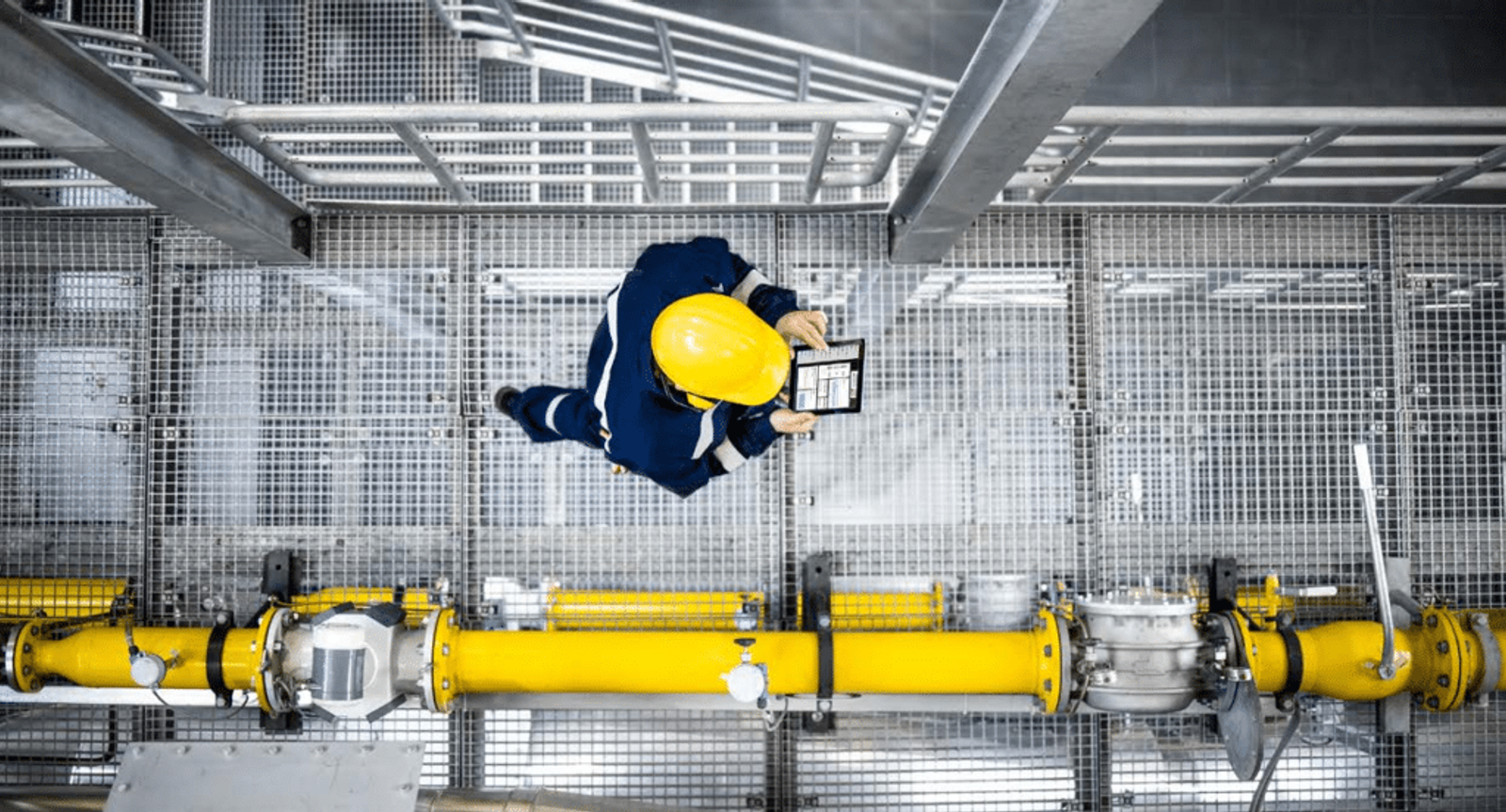 Technician with yellow hard hat and tablet inspecting yellow pump system from above