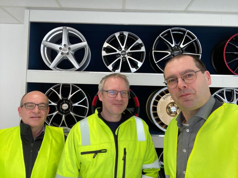 Drei Mitarbeiter in gelber Sicherheitsweste vor Felgen-Ausstellungswand bei Druckluft-Leckage-Projekt