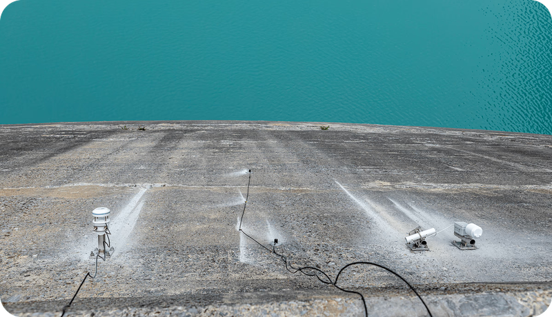 Auf dem Beton der Staumauer montierte Strahlungs- und Wettersensoren mit Kabeln, im Hintergrund die türkisfarbene Wasserfläche des Limmernsees