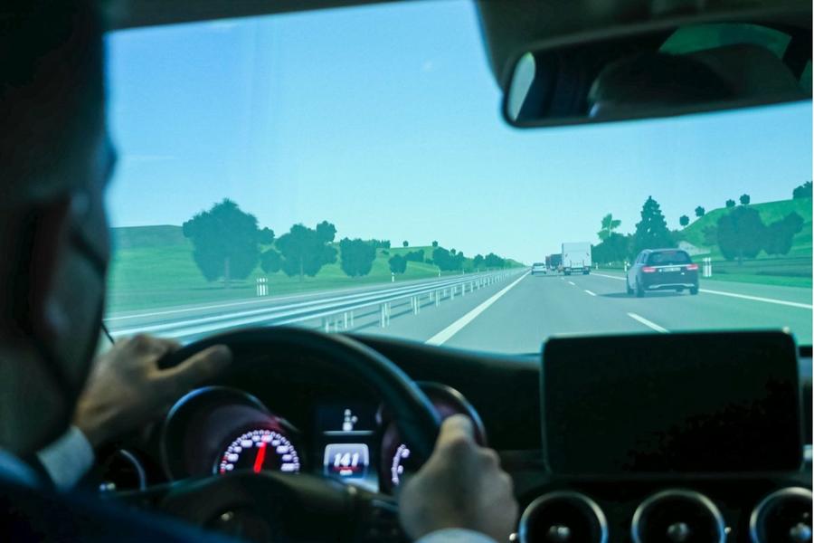 Blick aus dem Cockpit eines Fahrsimulators mit Händen am Lenkrad und simulierter Autobahn auf dem Bildschirm