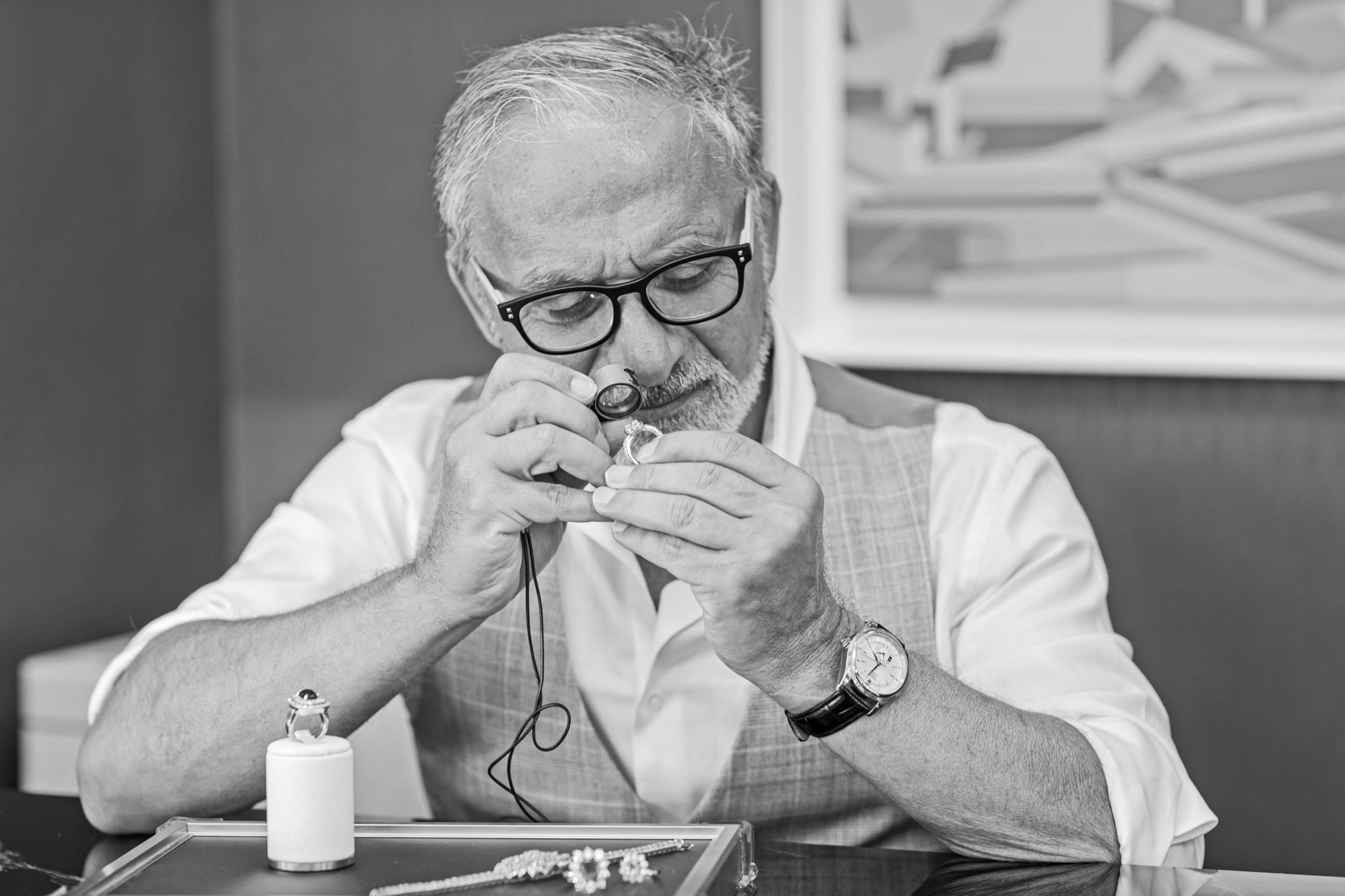 Jewellery expert examining a ring with a loupe, focusing on intricate details, with additional jewellery displayed nearby.