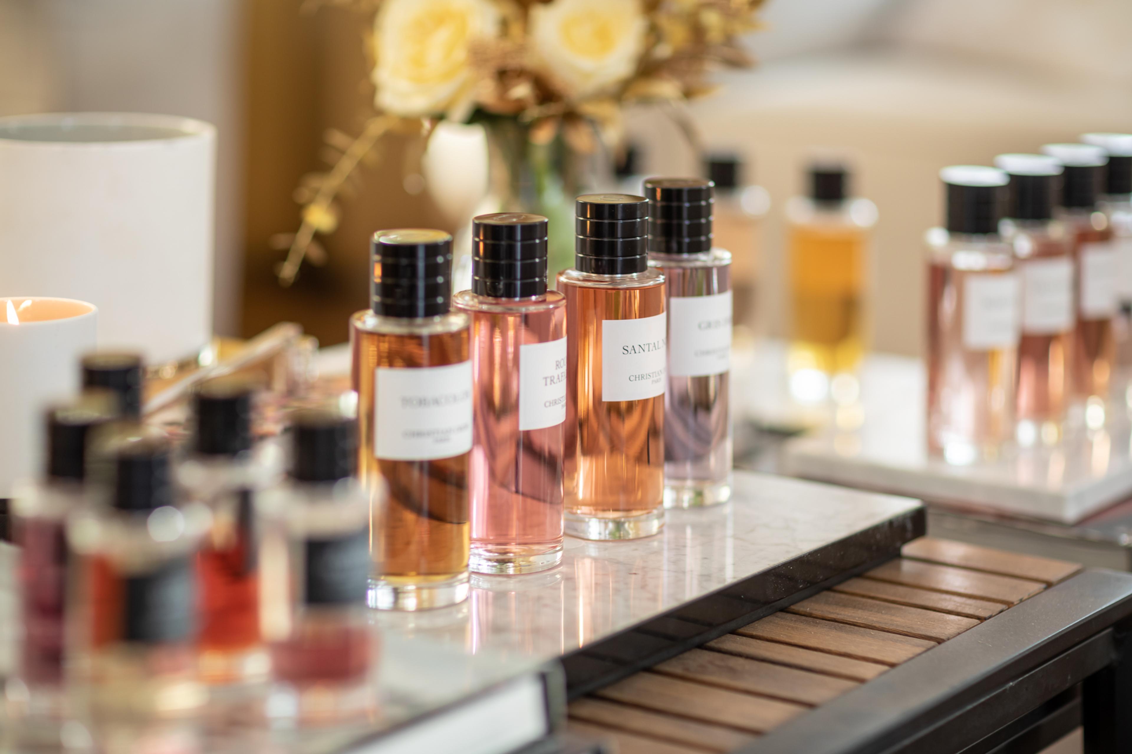 Luxury perfumes displayed on a marble tray with soft lighting, surrounded by flowers and a lit candle.