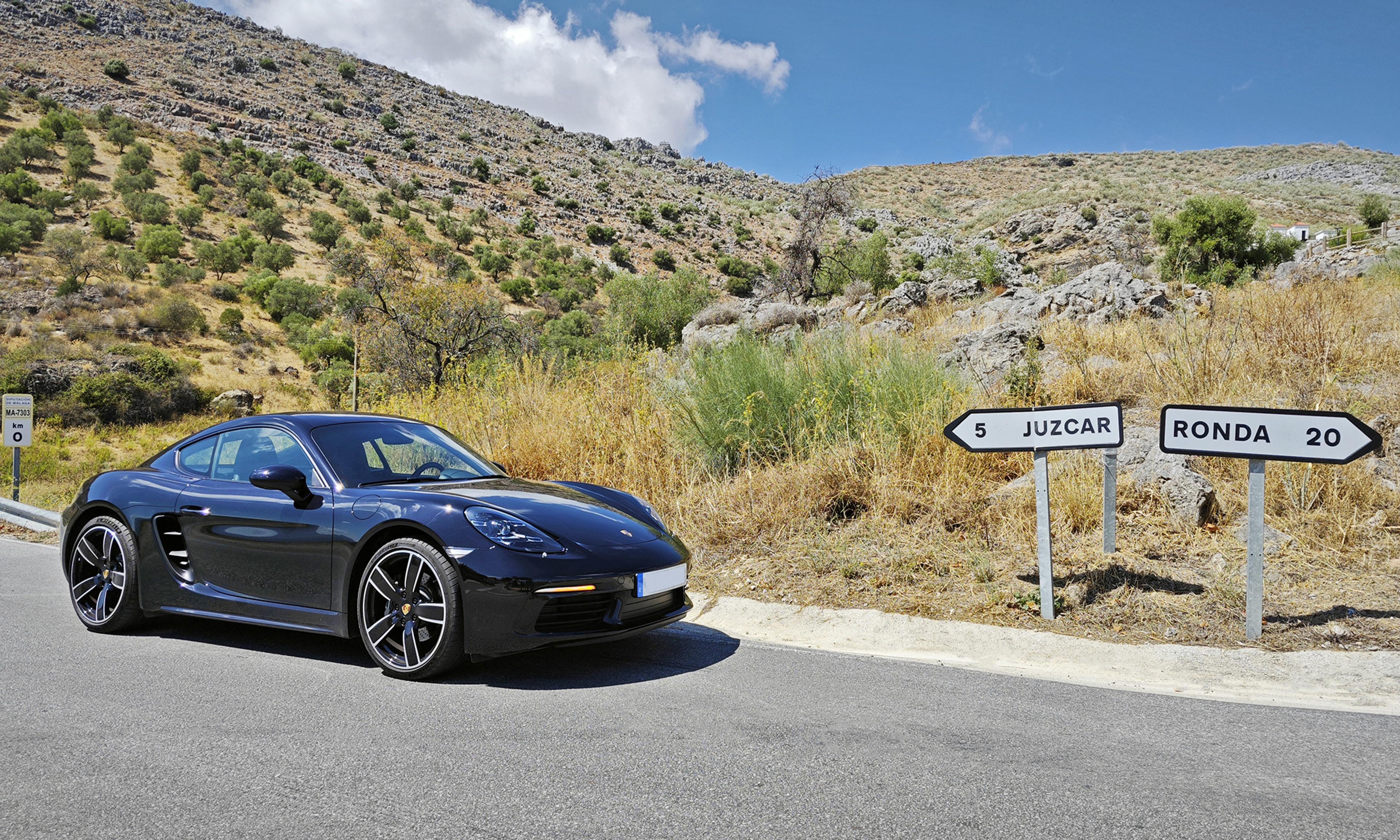 A sleek black sports car parked against a scenic rural backdrop, near road signs pointing to nearby places, surrounded by rolling hills and clear skies.
