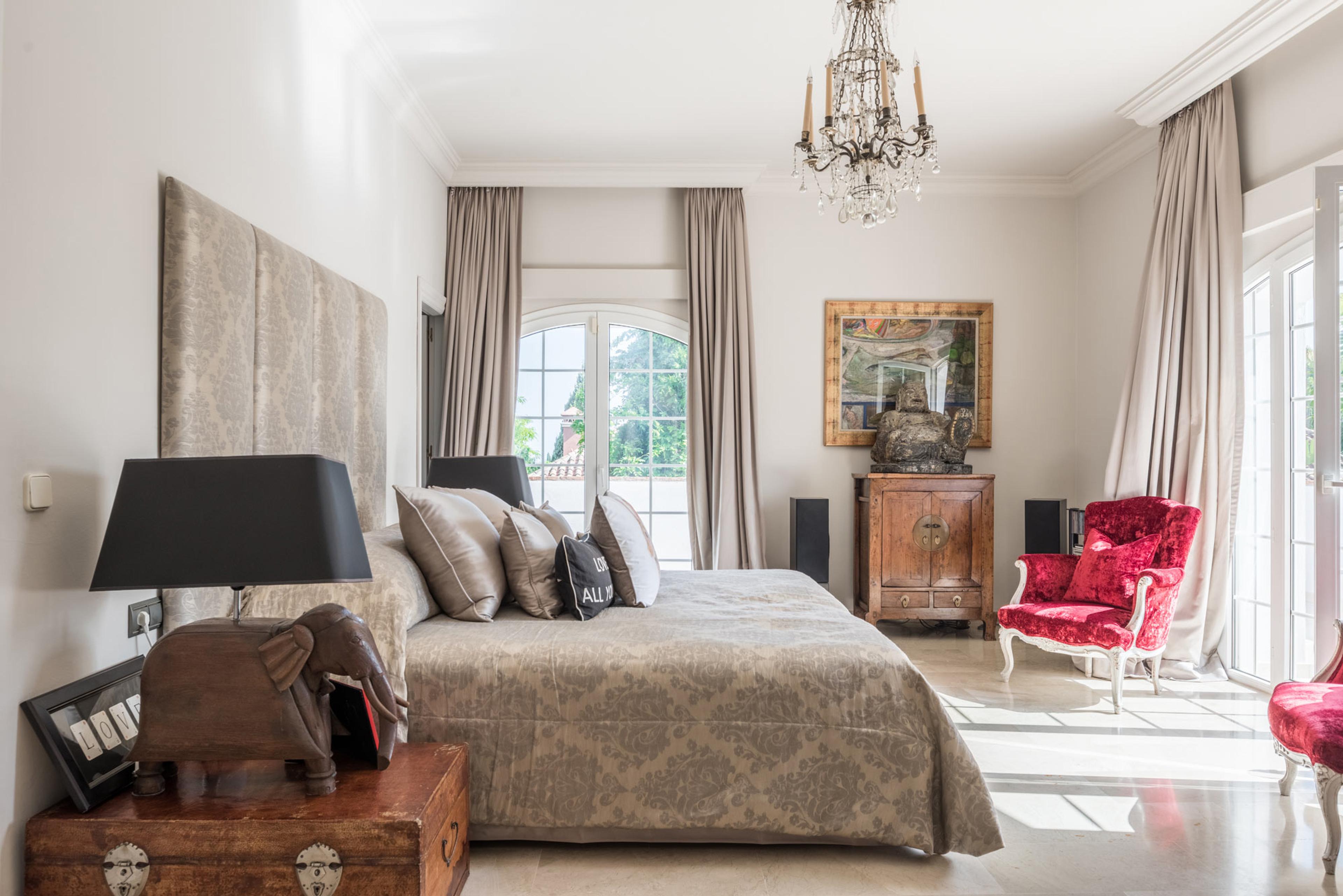 Elegant bedroom with a chandelier, red armchair, and decorative elephant lamp on a wooden side table.