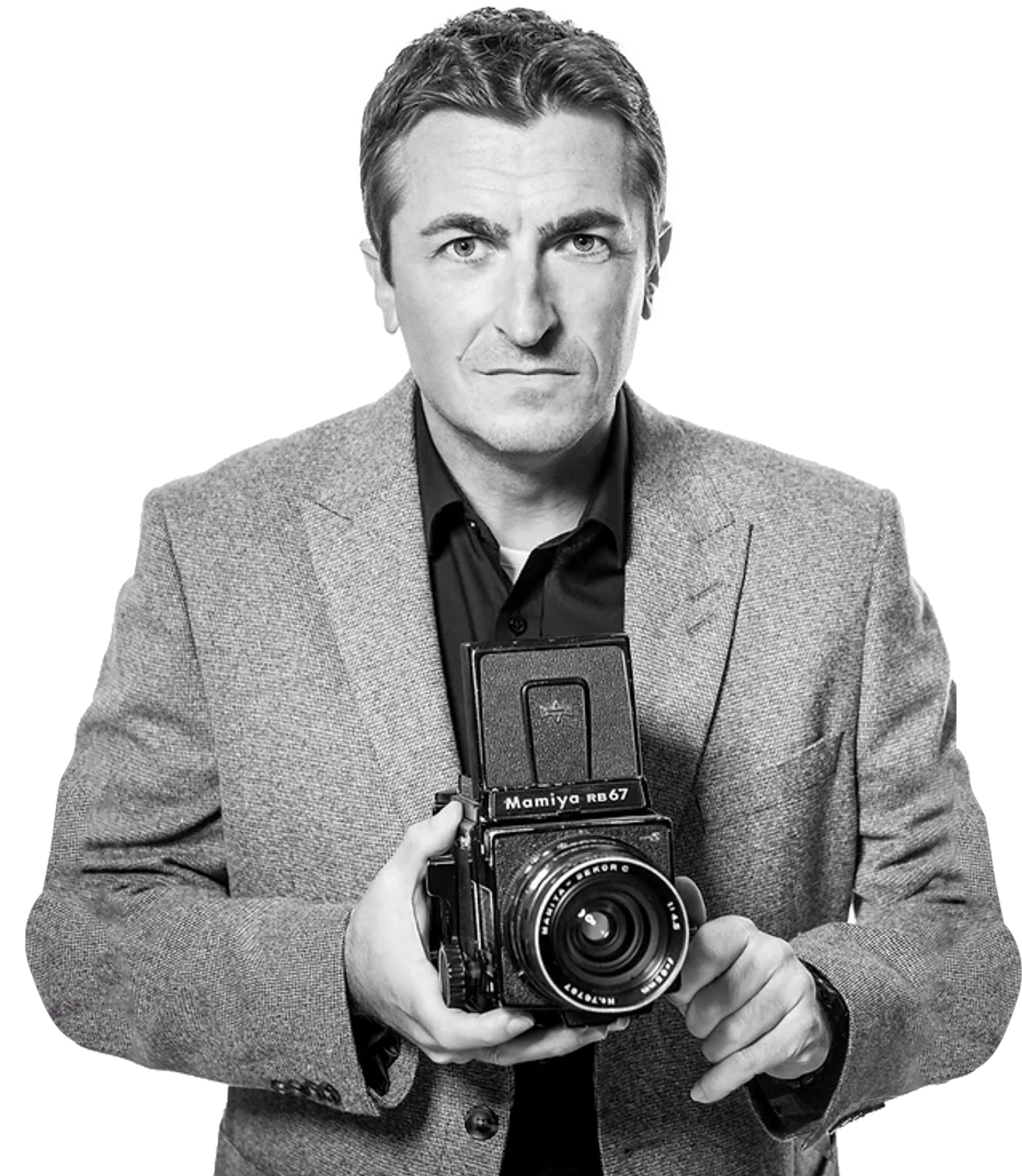 Black-and-white portrait of Gregory Korvin in a blazer holding a Mamiya RB67 camera, with a confident and professional demeanour.