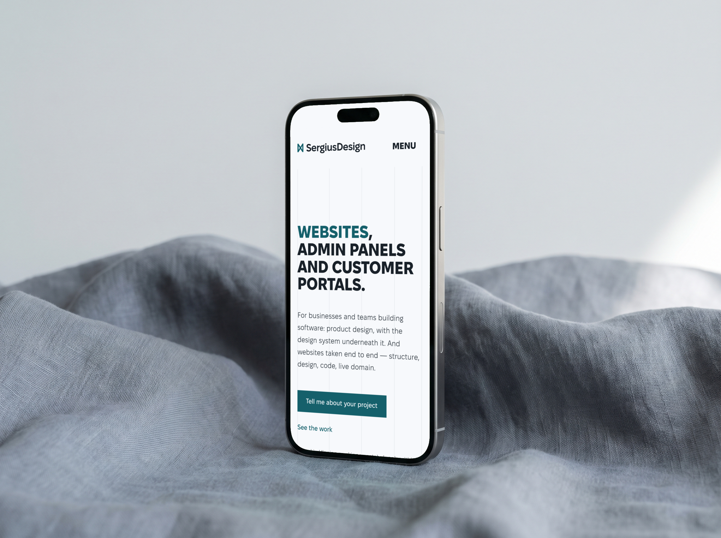 Телефон на сірій тканині з головною sergiusdesign.com англійською: заголовок «Websites, admin panels and customer portals» і кнопка «Tell me about your project»