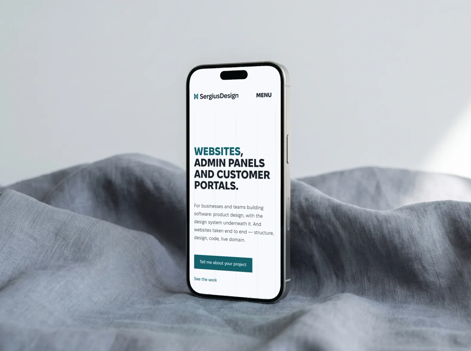 Телефон на сірій тканині з головною sergiusdesign.com англійською: заголовок «Websites, admin panels and customer portals» і кнопка «Tell me about your project»