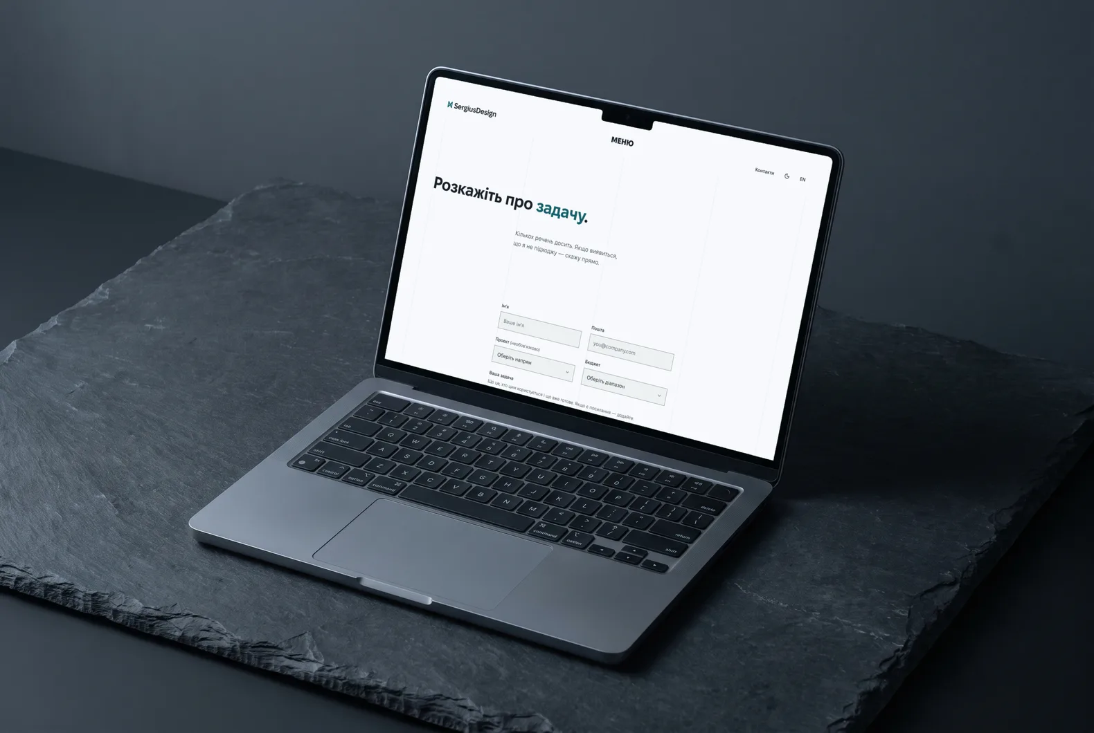 Ноутбук на темному сланці зі сторінкою контактів sergiusdesign.com: заголовок «Розкажіть про задачу» і коротка форма, світла тема