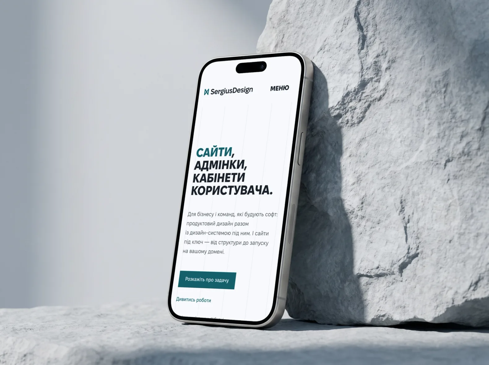 Телефон біля світлого каменя з головною sergiusdesign.com українською: заголовок «Сайти, адмінки, кабінети користувача» і кнопка «Розкажіть про задачу»