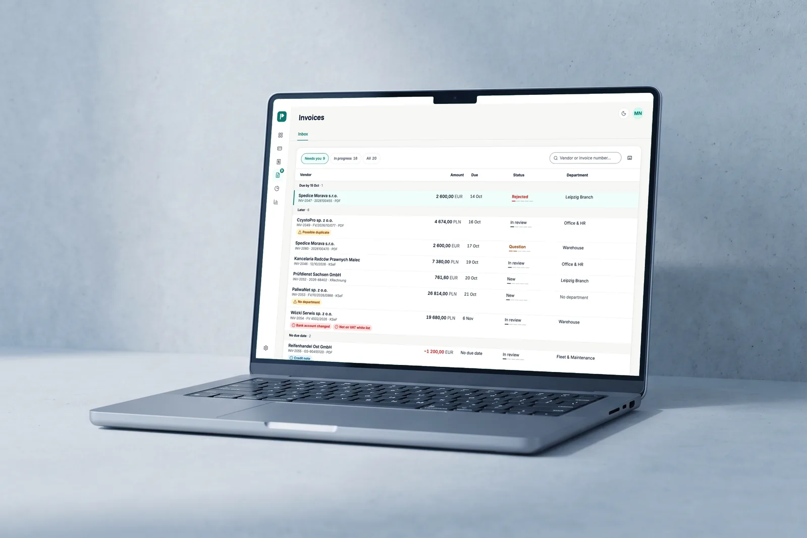 Laptop on pale concrete showing the Payvane invoice inbox: a list grouped by urgency with flags for a possible duplicate, no department and a changed bank account