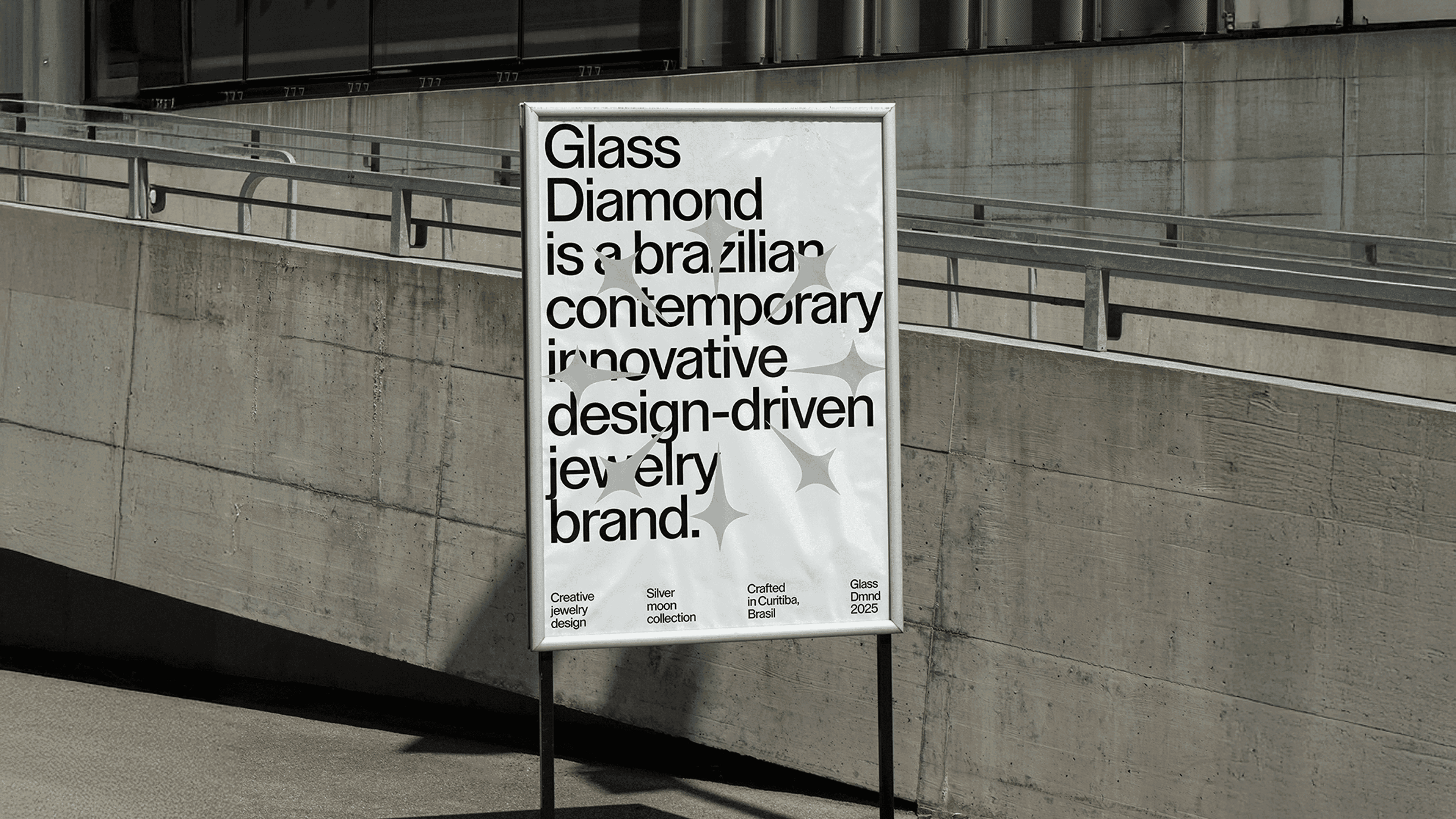 Cartaz do Glass Diamond num suporte diante de muro de concreto: 'a brazilian contemporary innovative design-driven jewelry brand'