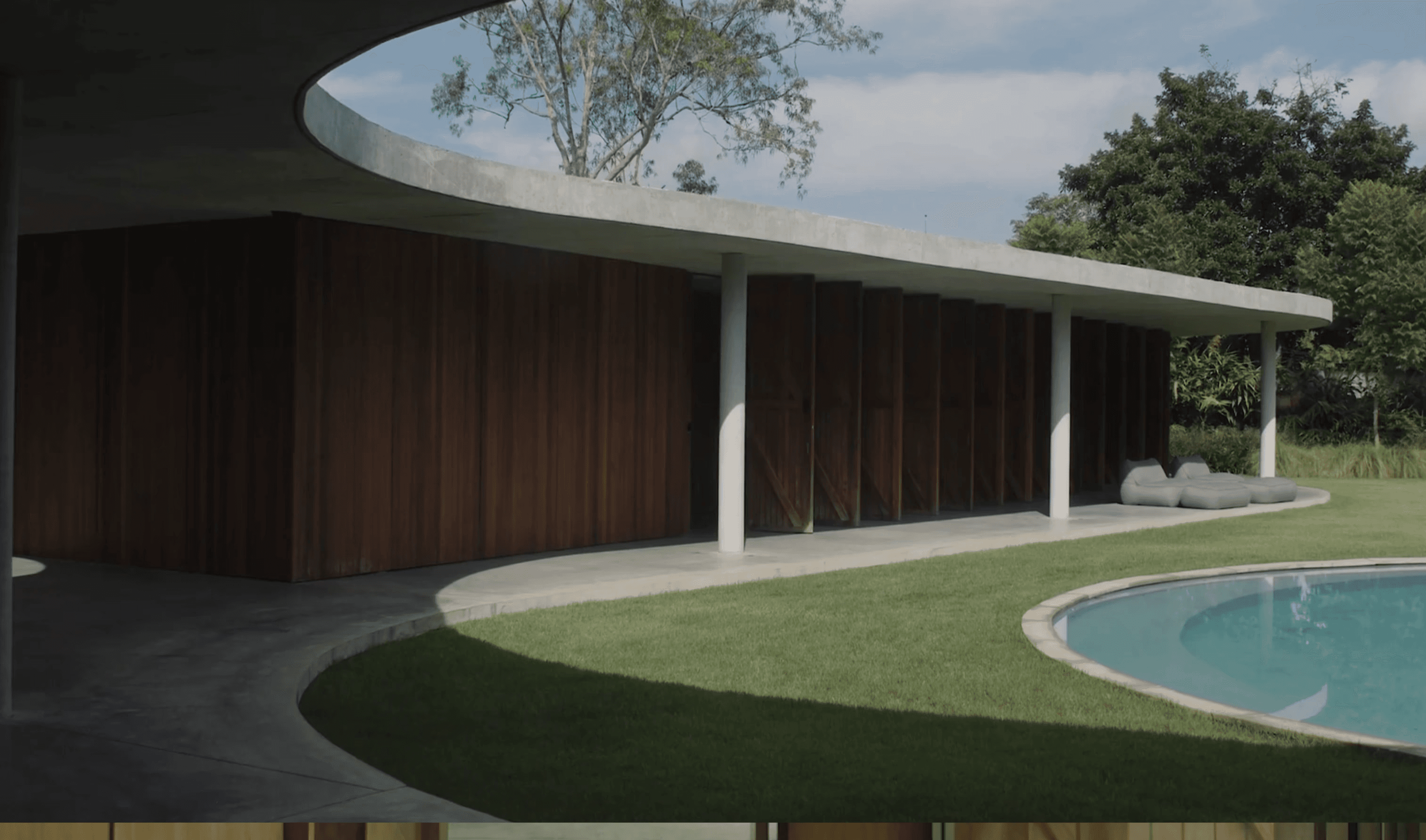 Casa moderna com laje curva de concreto e fachada de madeira ripada, gramado e piscina arredondada à frente