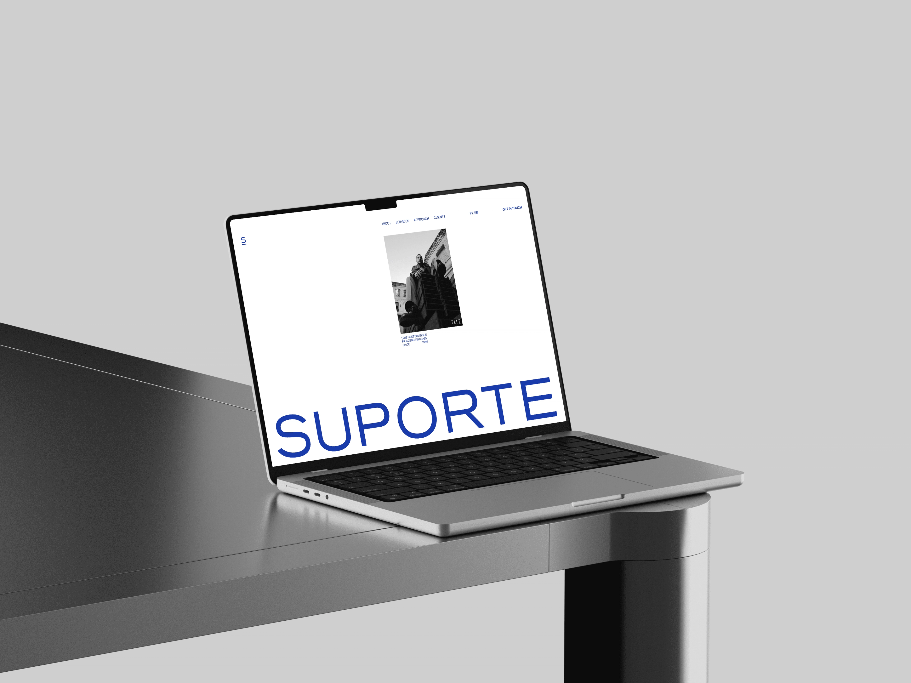 Notebook na quina de uma mesa cinza exibindo a home da Suporte, com o letreiro SUPORTE em azul ocupando a tela