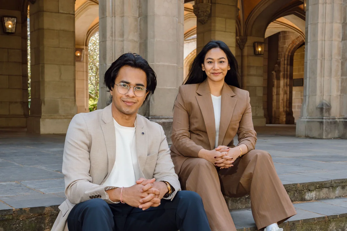 Syncrowin co-founders Jaideep Upadhyay and Aisshwarya Kansakaar seated on stone steps beneath sandstone arches in Melbourne