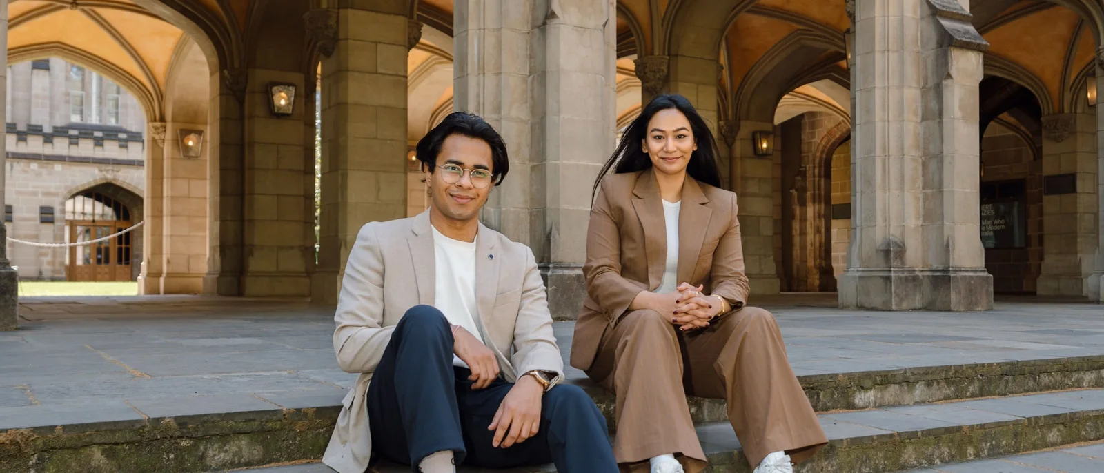 Syncrowin co-founders Jaideep Upadhyay and Aisshwarya Kansakaar seated on sandstone steps beneath a stone cloister