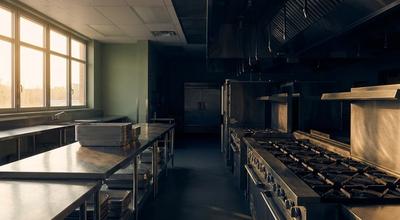 Empty commercial kitchen at dawn with unlit gas ranges, vent hoods, and stainless prep tables