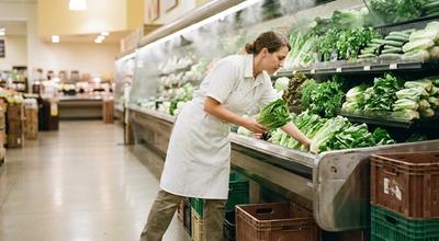 Grocery worker restocking romaine lettuce into a misted refrigerated produce case