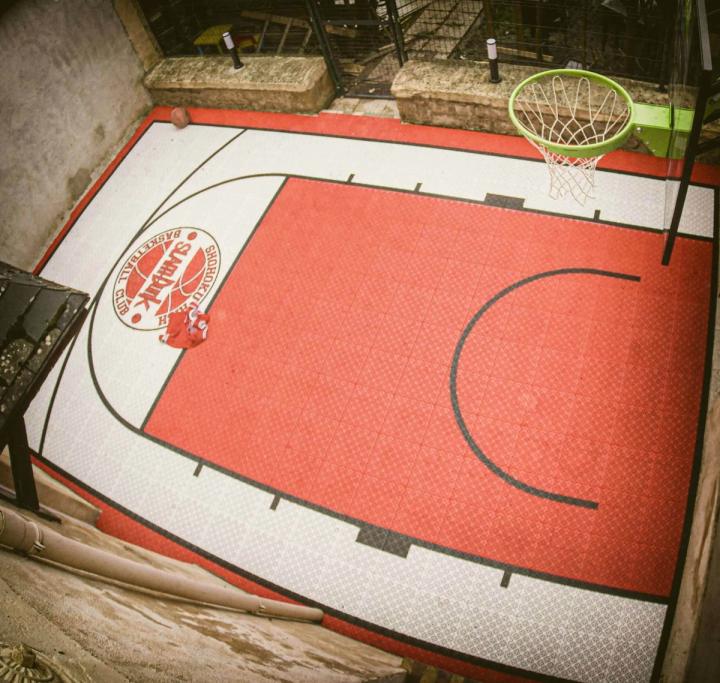 Demi-terrain de basket en dalles orange et blanches avec un logo de club peint au centre