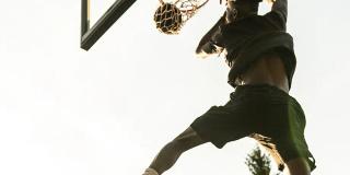 A player caught mid-dunk against a low sun, hanging from the rim of a MegaSlam hoop.