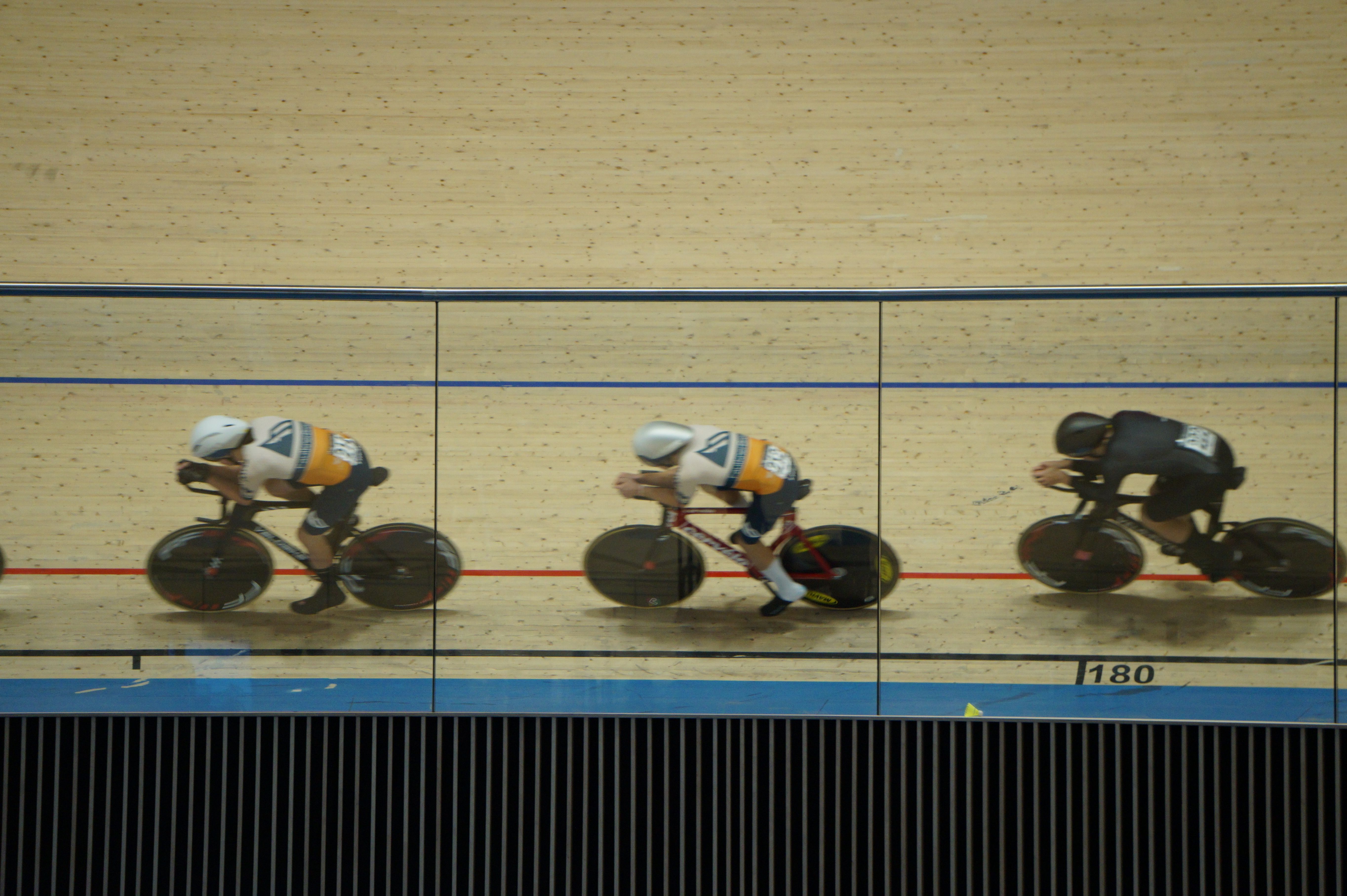 Three riders ride in line along the black line at the Alberta Velodrome