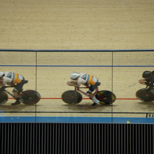 Three riders ride in line along the black line at the Alberta Velodrome