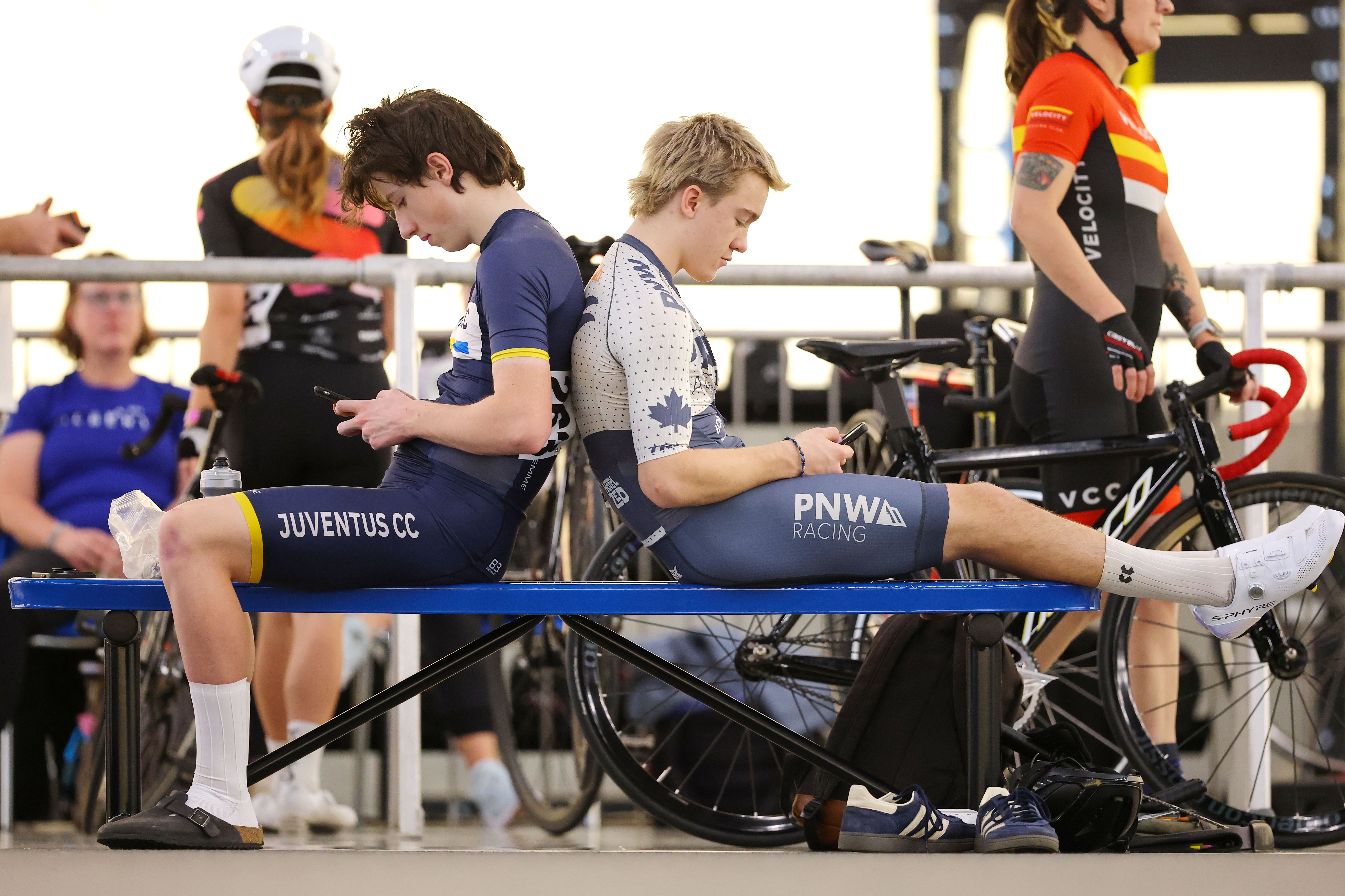 Two club riders in Juventus and PNW Racing kit sit back to back on a bench beside the track