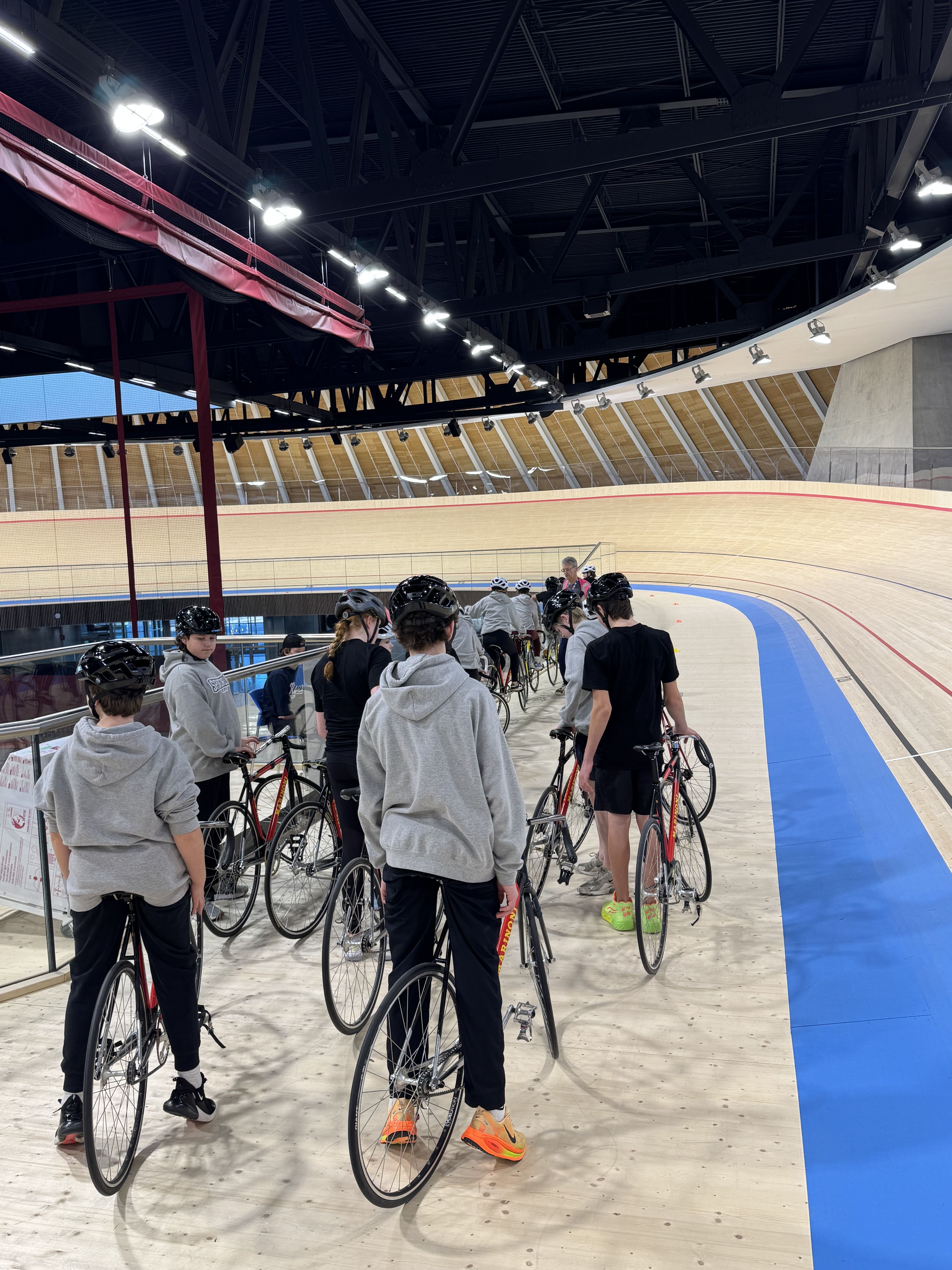 A school group walking their bikes onto the track with a coach