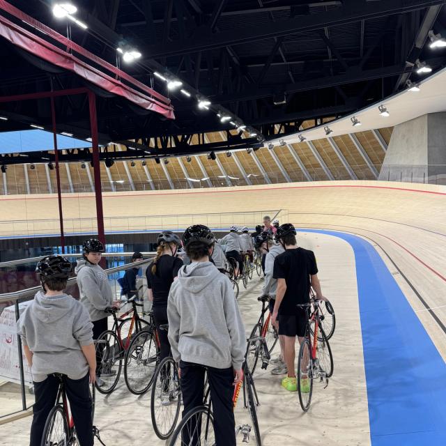 A school group walking their bikes onto the track with a coach