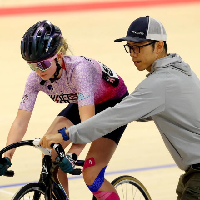 A coach holds a new rider steady on the track