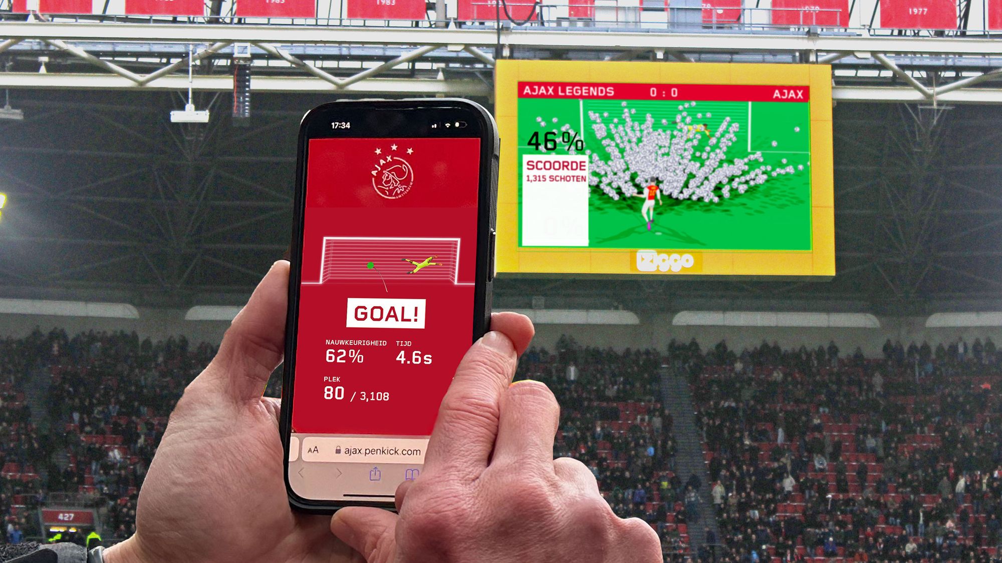Photograph of some hands holding a phone with a full stadium in the background. On the stadium's big screen a penalty is being taken with thousands of ball flying at the goal. The phone screen has an image of a goal and goal keeper with the word 'goal' and some stats below the image