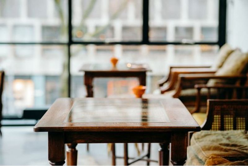 A close-up view of an empty, polished wooden table in what appears to be a restaurant or cafe setting. Other tables and chairs are visible but blurred in the background.
