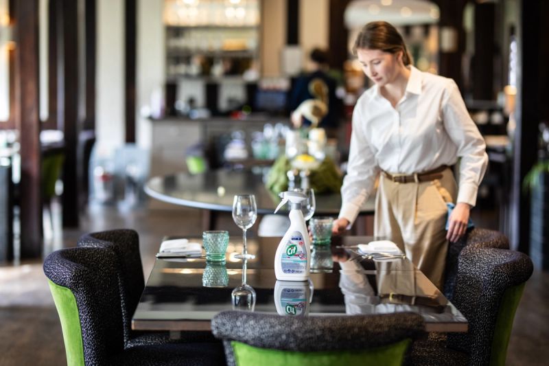 A woman cleans a restaurant table with Cif cleaner.