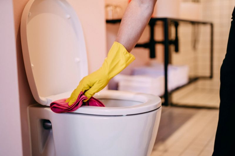 a person wearing yellow gloves is cleaning a toilet in a bathroom .
