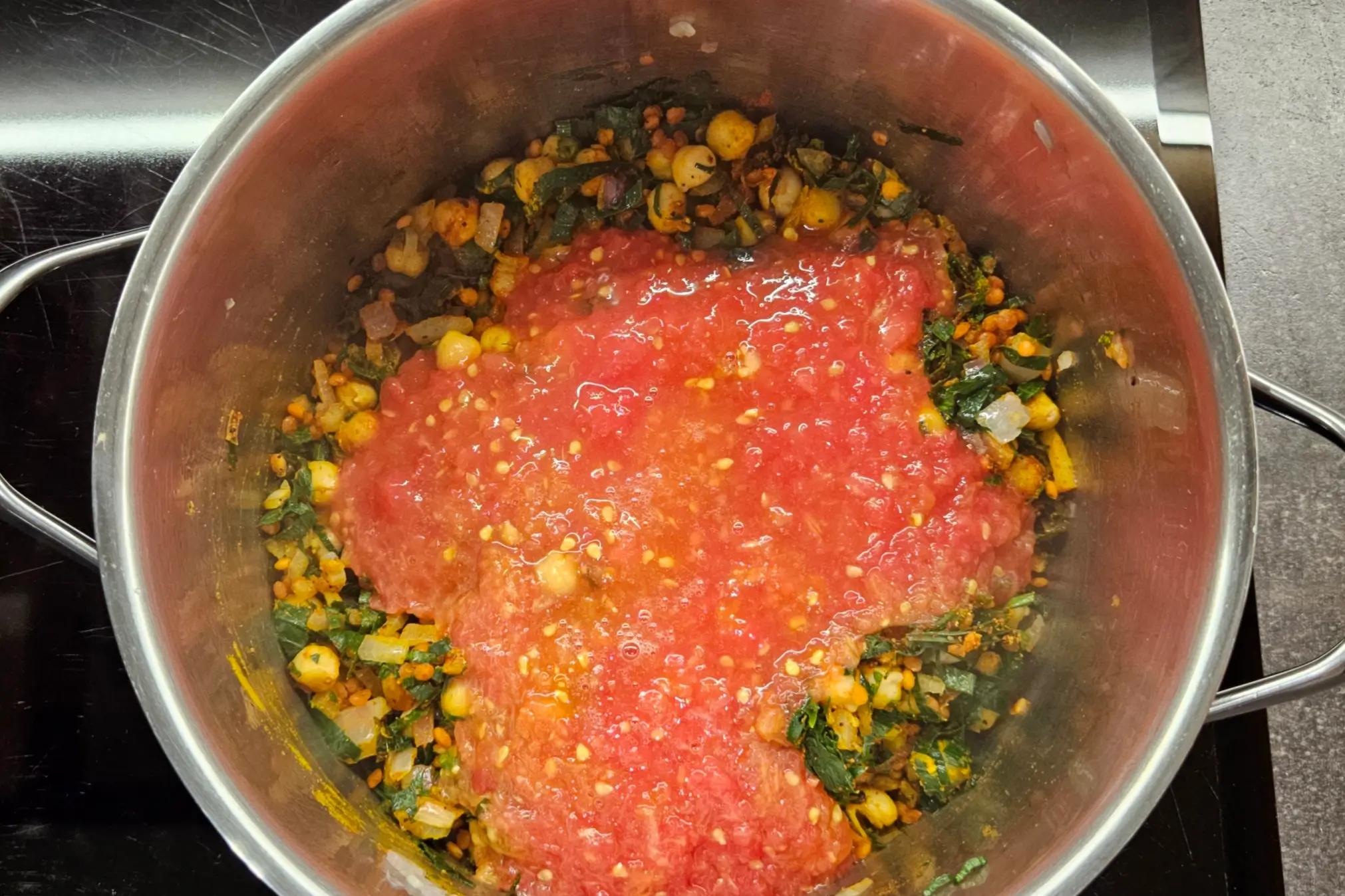 Grated fresh tomato pulp being poured into the Harira soup pot.
