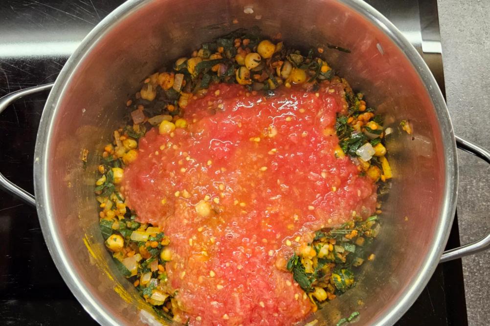 Grated fresh tomato pulp being poured into the Harira soup pot.