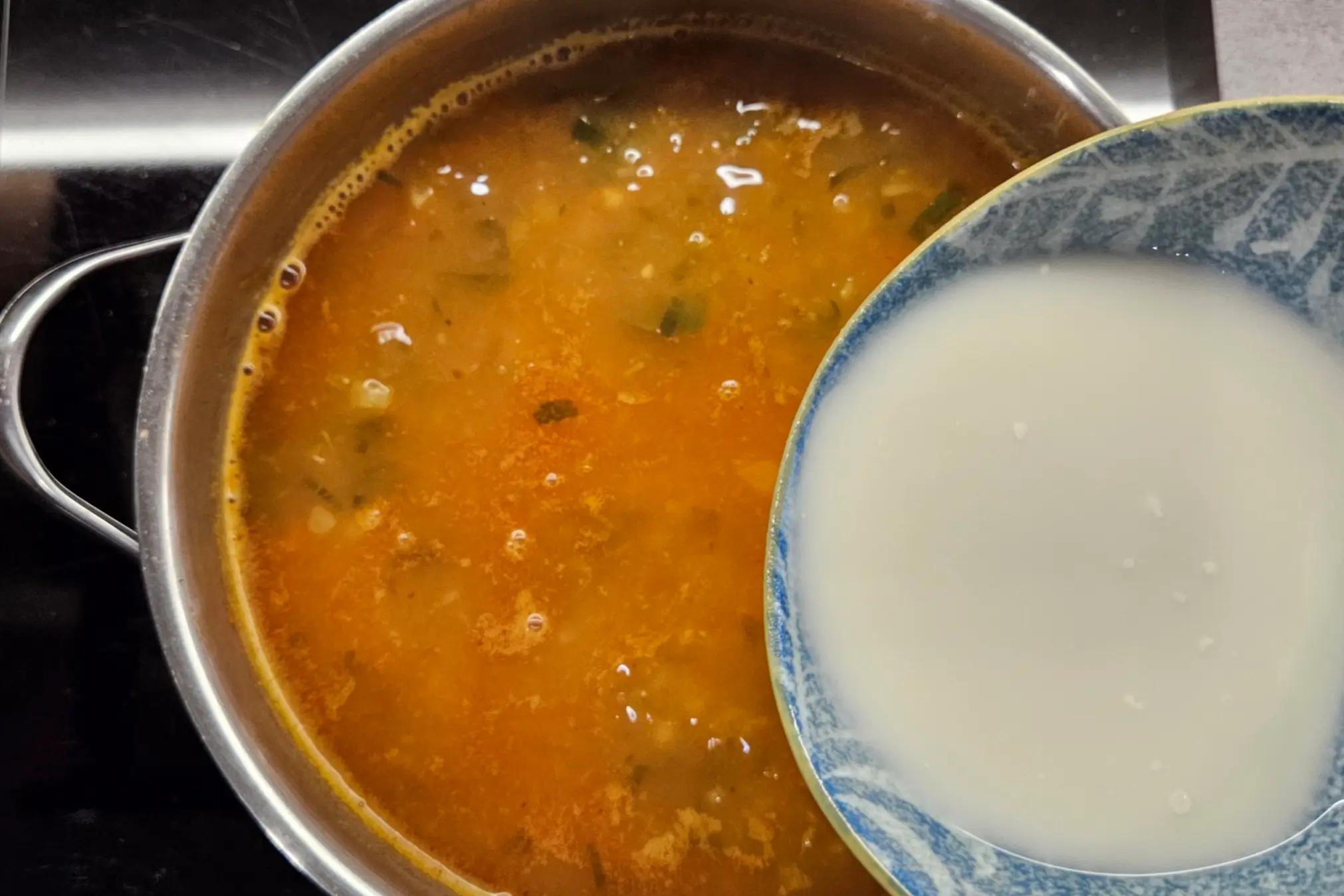 Whisking all-purpose flour with cold water in a bowl to create a smooth thickening slurry.