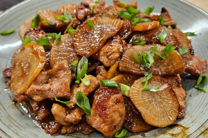 Страва з обсмажених шматочків м’яса та тонко нарізаного дайкону в карамелізованому соусі, посипана свіжою зеленою цибулею.
