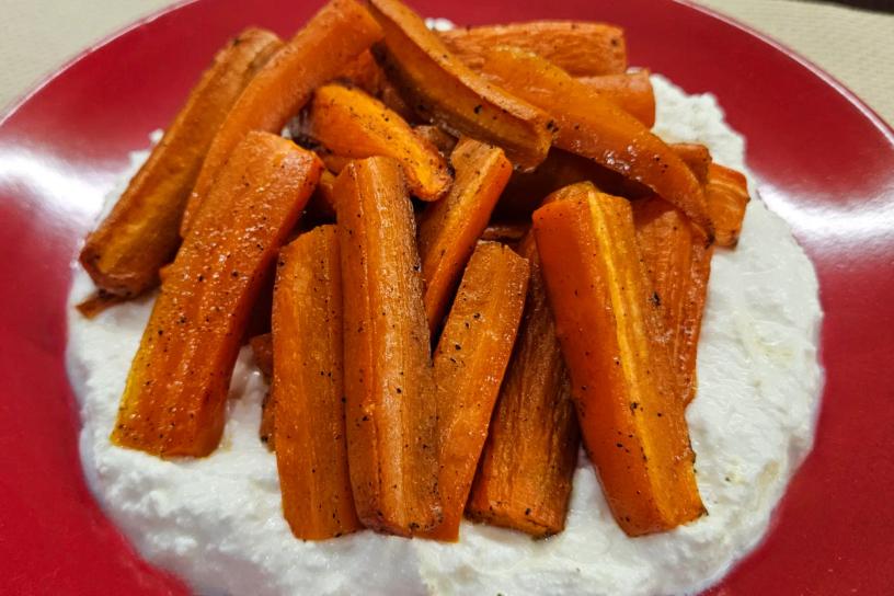 Roasted carrot chunks on a creamy white sauce, served on a red plate.