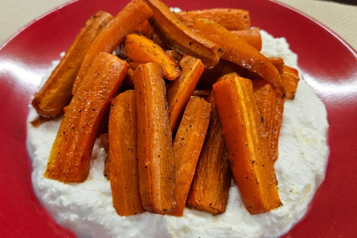 Roasted carrot chunks on a creamy white sauce, served on a red plate.
