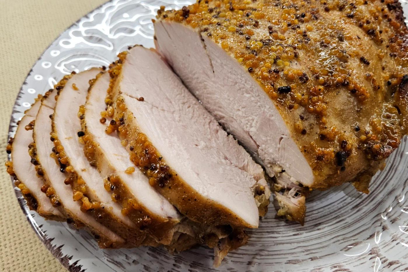 Нарізане філе індички з медово-гірчичною скоринкою та спеціями на декоративній тарілці. М’ясо світле й соковите всередині.