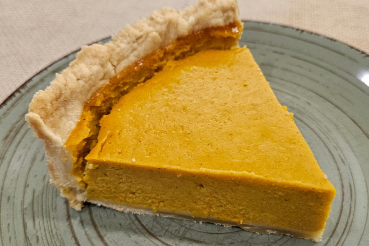 A close-up view of a pumpkin pie slice showing its smooth, creamy orange filling and delicate, flaky shortcrust base.