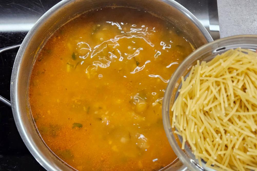 Adding vermicelli pasta into the boiling Harira soup while stirring with a spoon.
