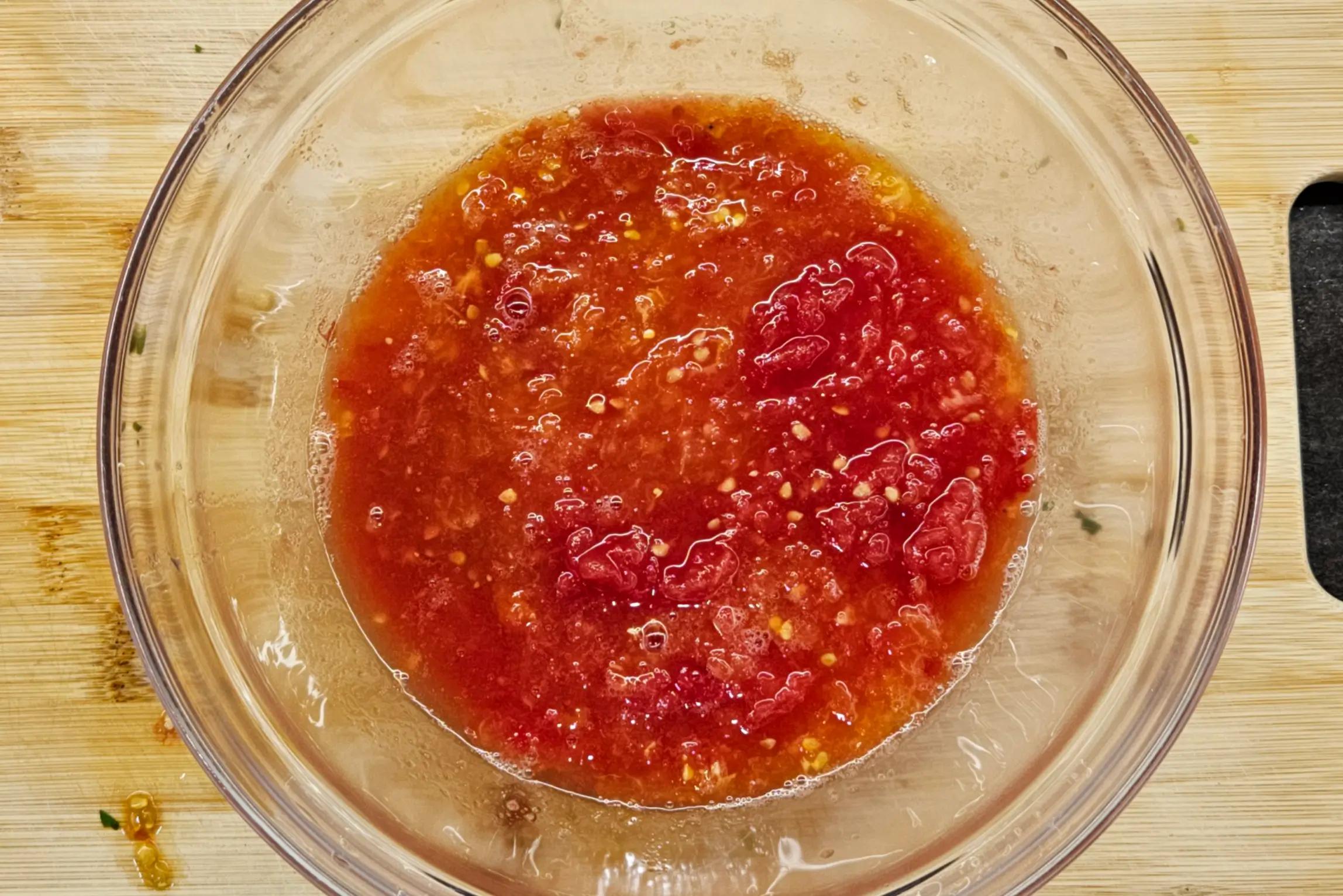 Fresh tomatoes being grated on the coarse side of a box grater into a bowl.