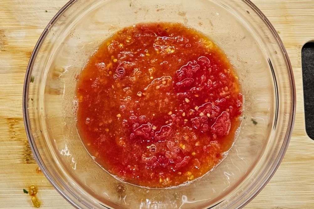 Fresh tomatoes being grated on the coarse side of a box grater into a bowl.