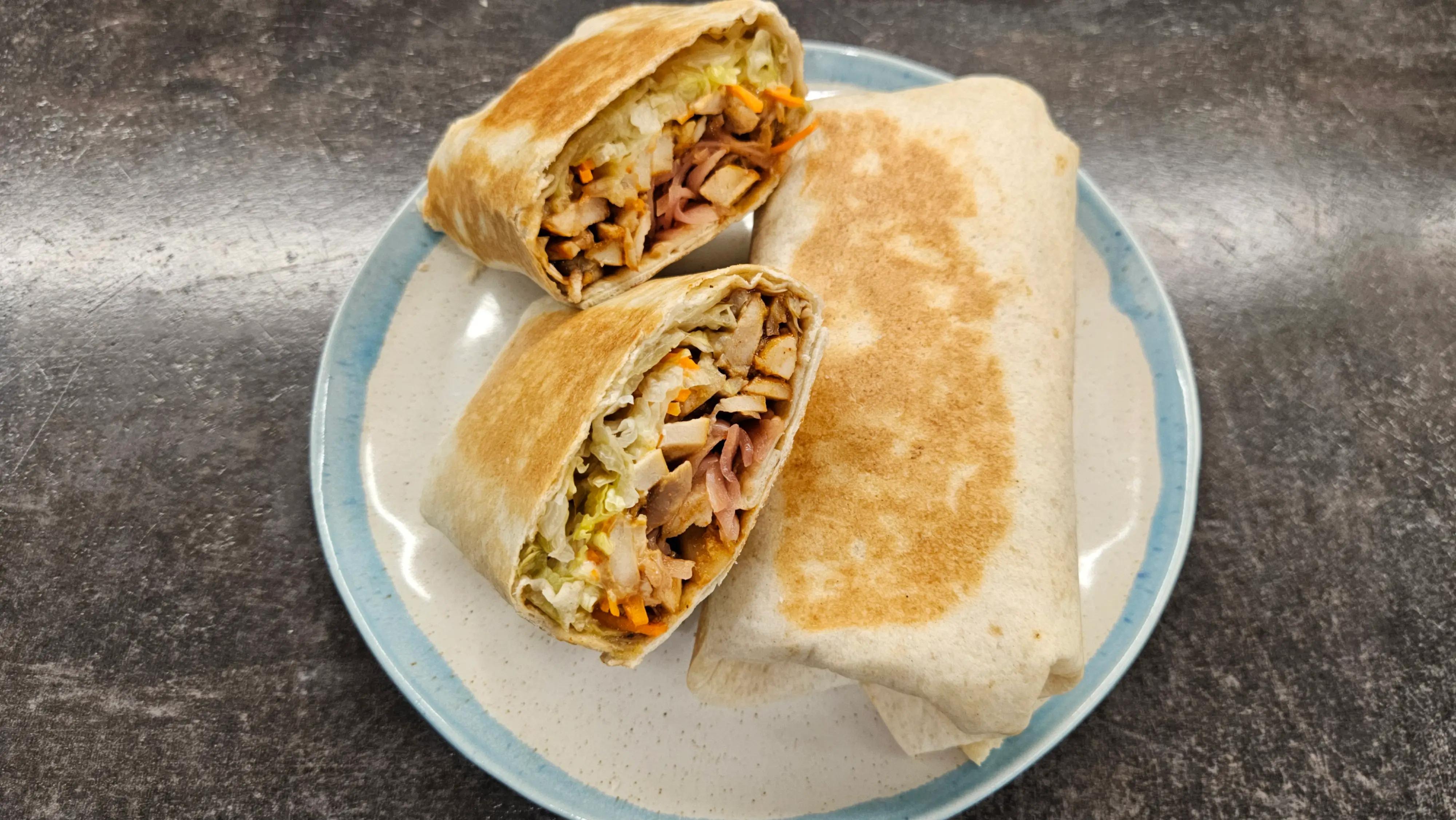 Шаурма з куркою, овочами та маринованою цибулею, розрізана навпіл на тарілці
