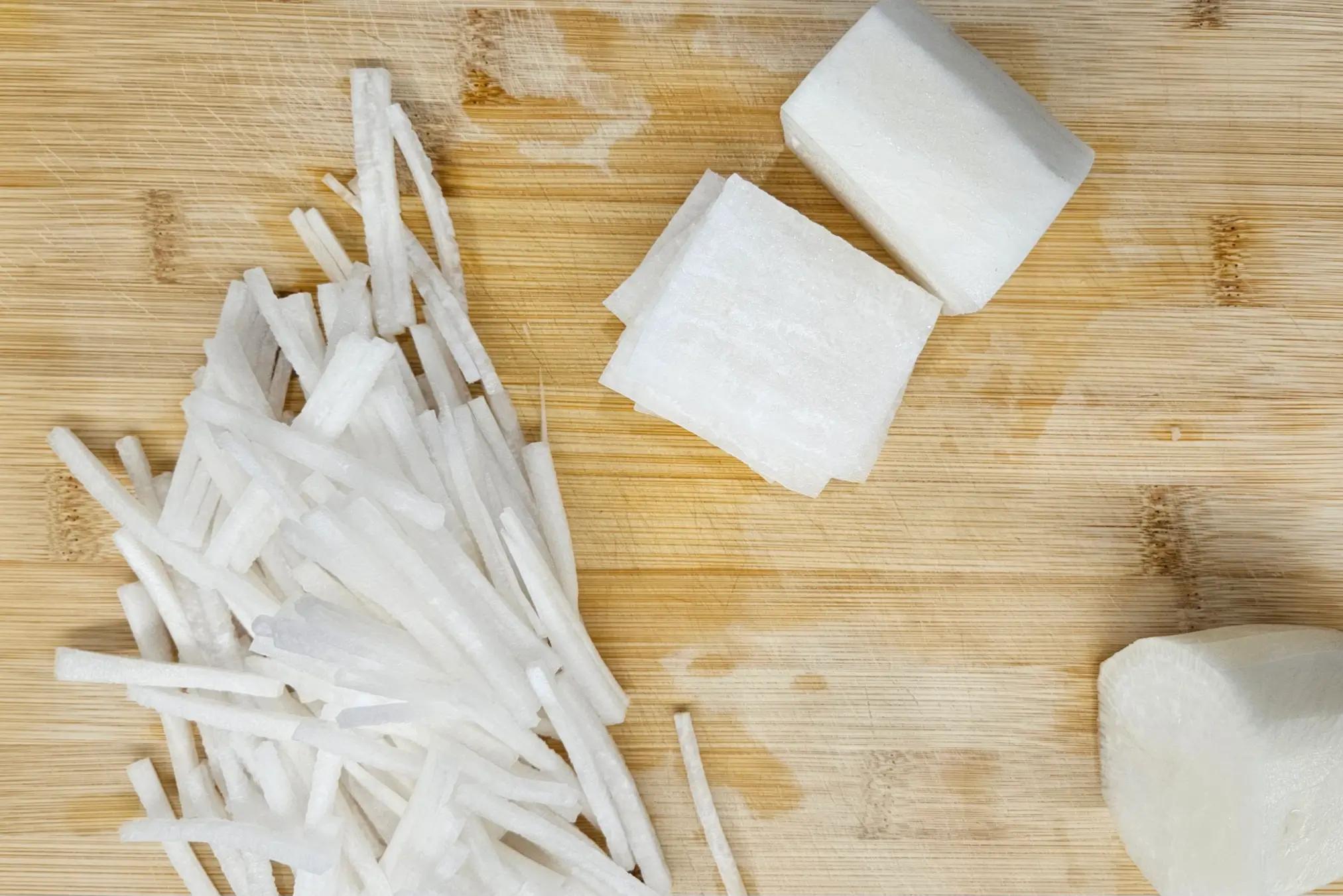 Julienned daikon radish matchsticks on a cutting board.