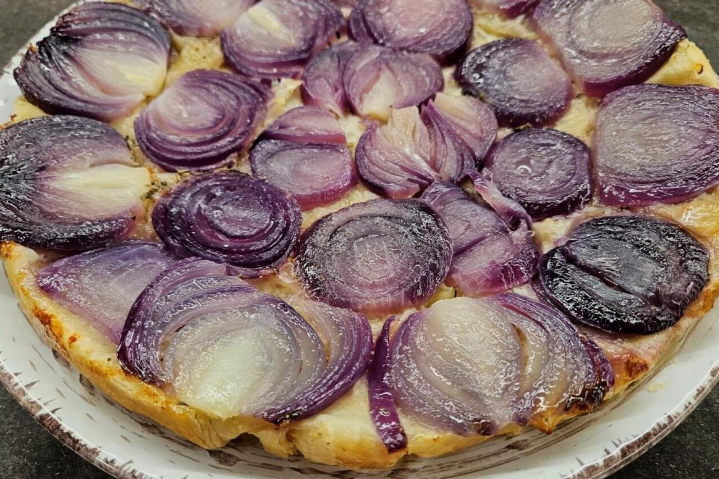 A caramelized onion upside-down tart with golden puff pastry, elegantly plated on a white dish.